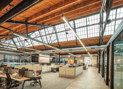 Spacious modern office with high wooden ceilings, large skylights, and open workspaces. Bright and airy atmosphere evokes productivity.