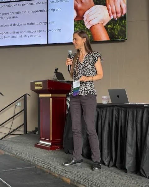 Gina Oswald holding a microphone while on stage delivering keynote address.