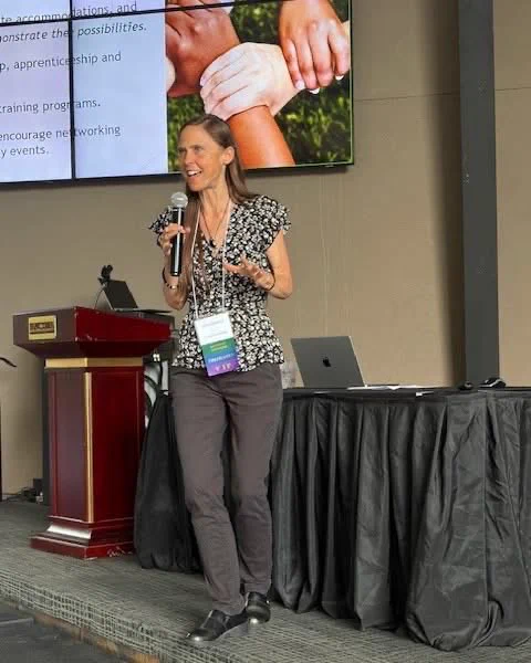 Gina Oswald speaking on stage at a conference.