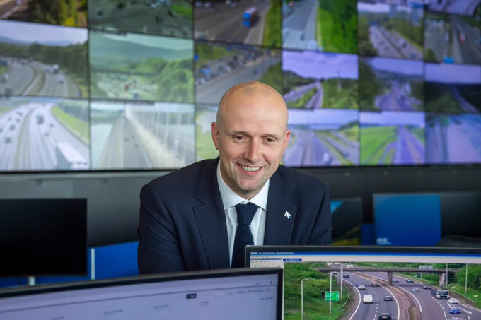 Transport Secretary Stephen Flynn smiles for a photo at the Traffic Scotland National Control Centre. Many monitors in the background show live footage from Scotland's trunk road network.