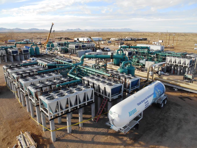 A large geothermal facility located in a desert environment, with mountains visible in the background.