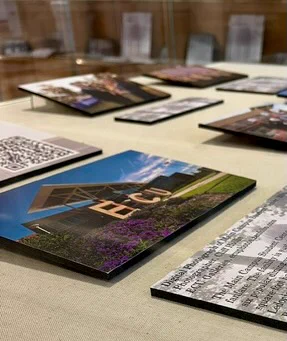 Art display featuring various photos on a table, including an image with three large letters on a building surrounded by flowers.