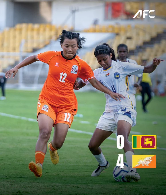 An intense moment during a women's football match between teams in orange and white jerseys. The score prominently displayed shows 4-0 with one player from each team in a competitive tussle for control.