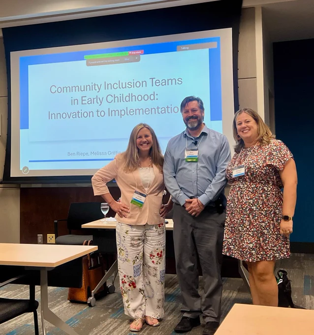 Image of three people posing in front of a presentation screen at the International Early Childhood Inclusion Institute.