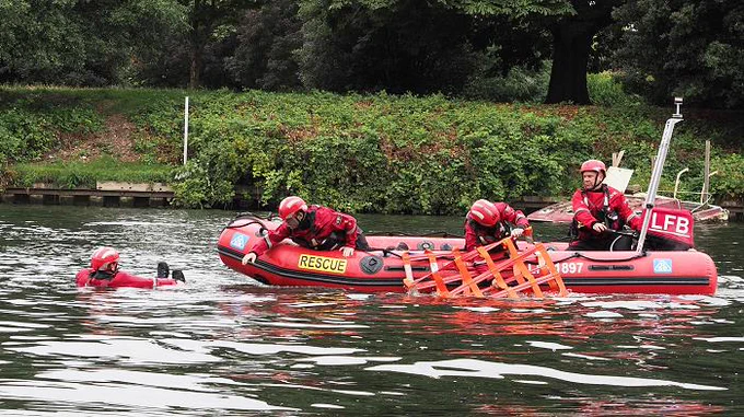 A firefighter is in the water and is rescued by a rescue boat crew as part of a training exercise.