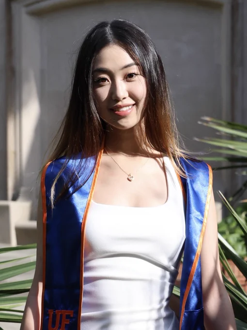 Anna poses in white dress outside for grad photo with uf regalia