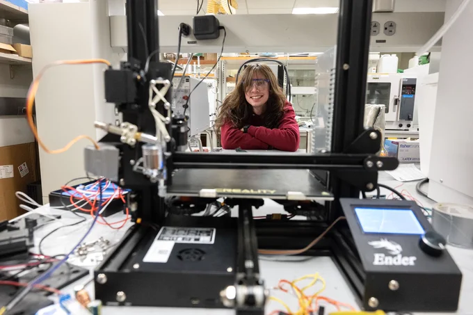 Jonathon (Jack) Bender in a lab, framed by his converted 3D printer.