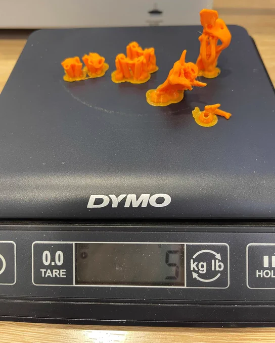 Small orange 3D-printed models sit on a digital scale after being printed.