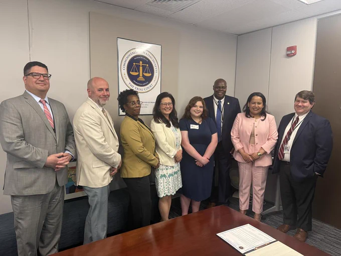 Group photo of Massachusetts Probation Service leadership, court staff, and a student participant during the “Co-Commissioner for the Day” program inside a conference room at Probation headquarters.