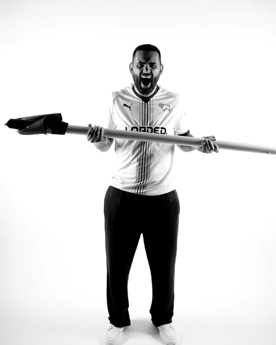 Bradley Johnson roars into the camera while brandishing a corner flag in celebration, while modelling the new Derby County 2026/27 PUMA home kit.
