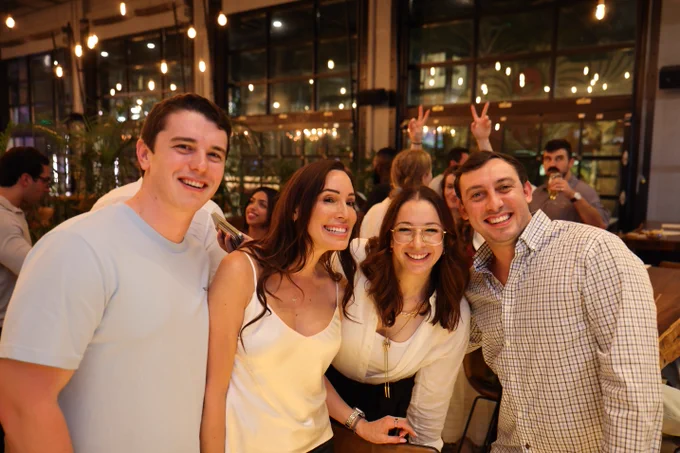A group of four coworkers smile for a photo at a fancy restaurant at night. Lights illuminate the ceiling.