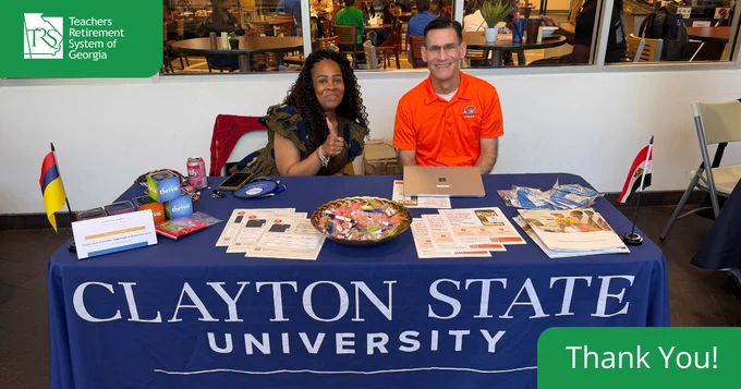 Two Clayton State University representatives seated at a table with informational brochures and a candy bowl at their 2026 spring wellness fair.