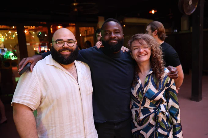 Three coworkers smile at a fancy outdoor nightspot. They are dressed up for a night out.
