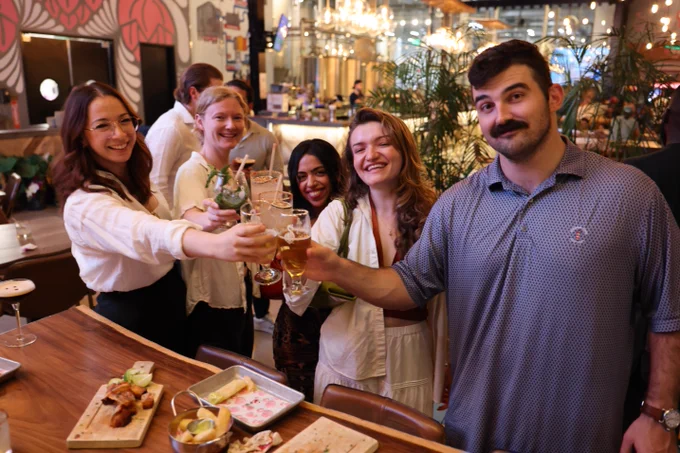 A group of five coworkers cheer their drinks for a photo.