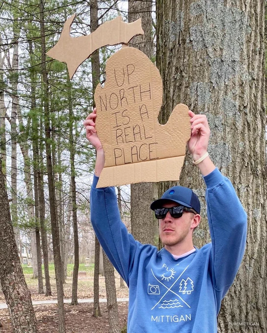 Person holding a cardboard cutout of Michigan with handwritten text that reads Up North is a real place