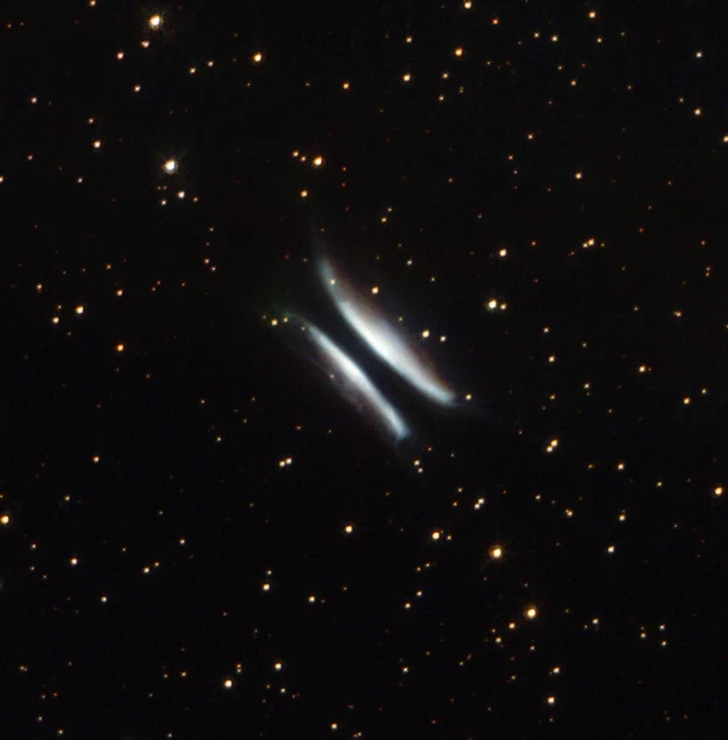 Two glowing white lobes of cosmic material shine on either side of a dark black disk of dust, loosely resembling a hamburger. The black background of space is dotted with several stars.

