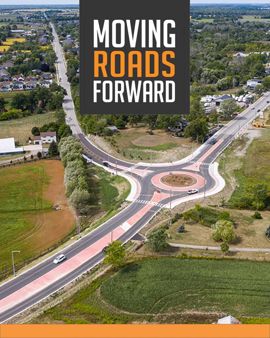 Aerial view of a roundabout intersection with the text "Moving Roads Forward".