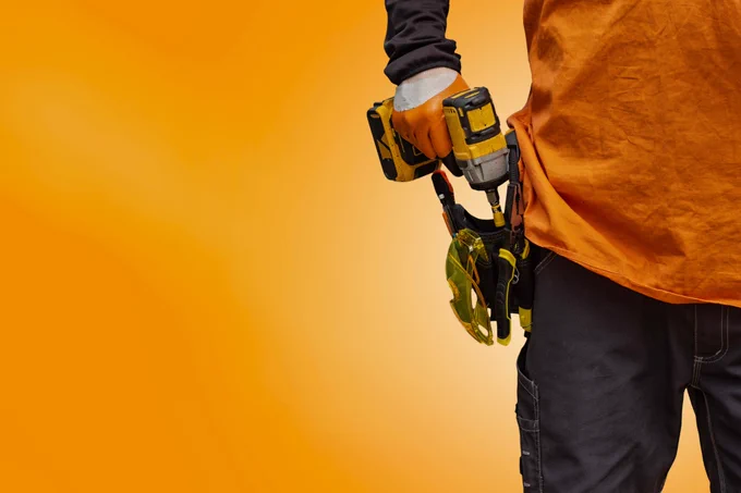 A stock image of a worker with an electric drill against an orange background.