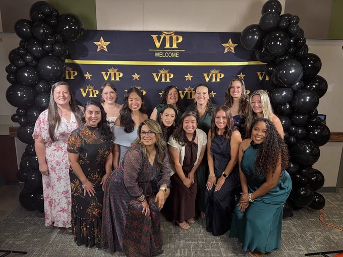 A group of women pose for a photo in front of a backdrop with balloons and the text "VIP Welcome".