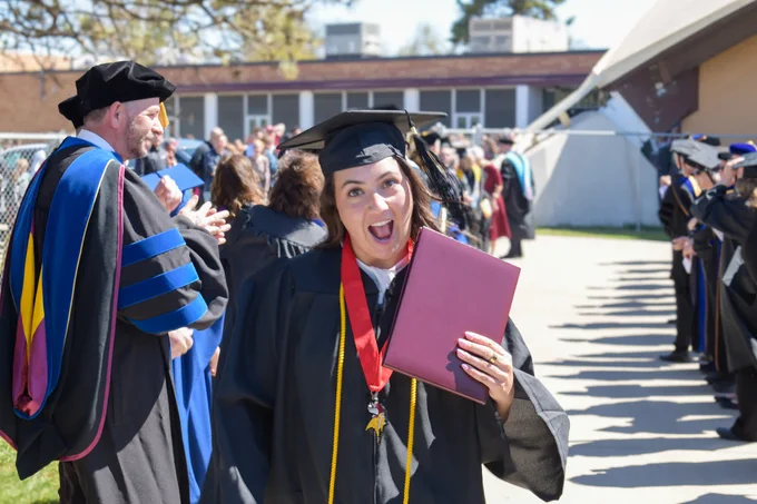 Hanna walking out of graduation in cap and gown with diploma in hand, faculty clapping behind her