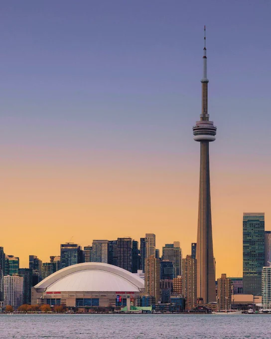 Toronto skyline at sunset featuring the CN Tower and Rogers Centre by the waterfront.