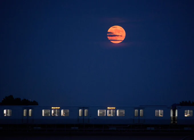 A reddish Moon, with clouds passing in front of it, floats above a quickly-moving subway train at night. Credit: NASA/Bill Ingalls