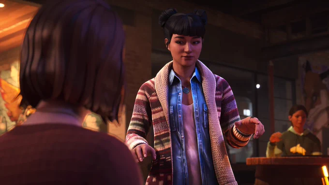 Amanda Thomas from Life is Strange: Double Exposure, an Indigenous woman of Cherokee and Algonquin descent, sharing a subtle, flirtatious moment with Max Caulfield inside her Lakeport bar, The Snapping Turtle. Amanda is standing by a table after serving a drink, looking towards Max with a playful smile and expressive hand gestures as she pauses, deciding to flirt. She is styled in her signature space buns with blunt bangs, wearing a blue denim shirt, a striped patterned knit cardigan, and a turquoise pendant necklace. Max is captured from behind in the left foreground, out of focus. The warm, atmospheric lighting of the bar illuminates Amanda, while another patron is softly blurred in the background on the right.