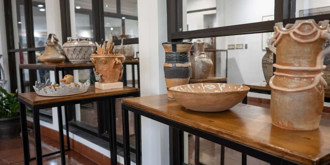Wooden tables displaying various handcrafted ceramic pots and bowls in a bright gallery space with glass partitions.