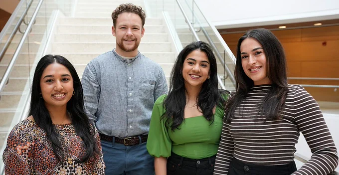 Four UMass Chan Medical School students stand together at the bottom of a stairway inside a building on campus. 