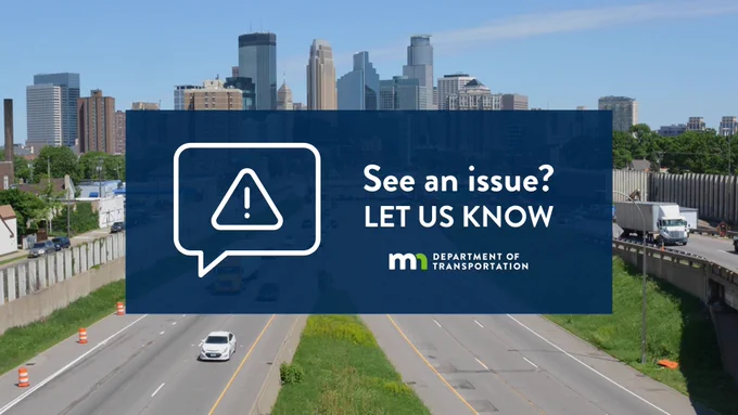 A northbound view of I-35W approaching the downtown Minneapolis skyline on a sunny day. A navy box features an alert icon and text reads, "See an issue? Let us know," next to the Minnesota Department of Transportation logo. Traffic barrels and vehicles are visible on the road.