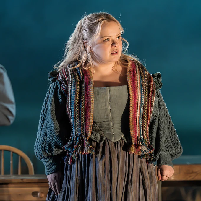 Nicola Coughlan stands in a pub wearing a green dress and bright shawl.