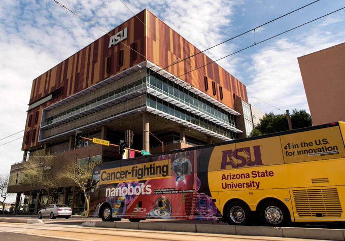 Arizona State University building with a branded shuttle bus promoting cancer-fighting nanobots parked in front on a sunny day.