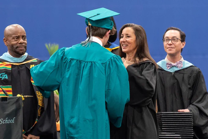 Four people in graduation gowns and caps, celebrating a graduation.