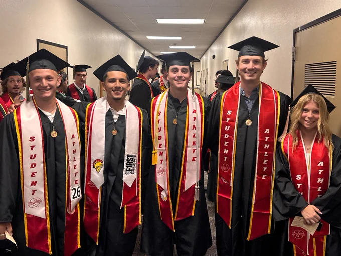 5 Stan State graduates standing in a hallway hiding from the rain.