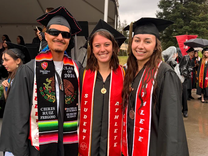Three Stan State athletes posing outdoors at commencement.