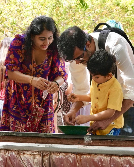 A family of three engaged in a hands-on activity outdoors, with the child focused on a gold panning pan while the parents assist.