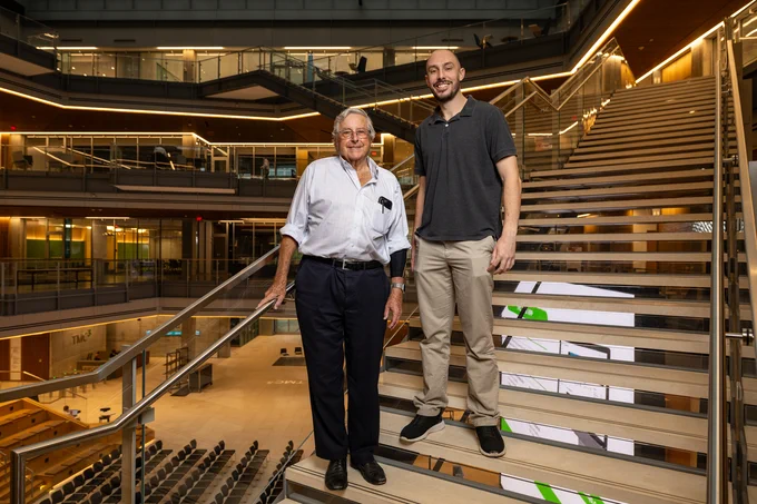 Peter J.A. Davies and Vicente Rubio stand on stairs inside the TMC3 Collaborative Building in Houston, Texas.