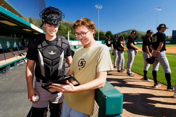 Gabe Riedel, right, consults with a Cal Poly baseball player during practice as teammates stand in the background.