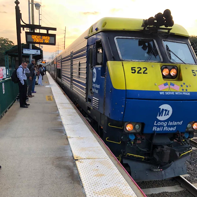 An LIRR diesel train pulling into Great River station as people wait on the platform.
