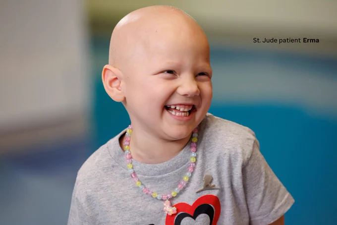 St. Jude patient Erma, pictured smiling to the side. Her gray shirt reads “I (heart shape) St. Jude”. She is also wearing a necklace.