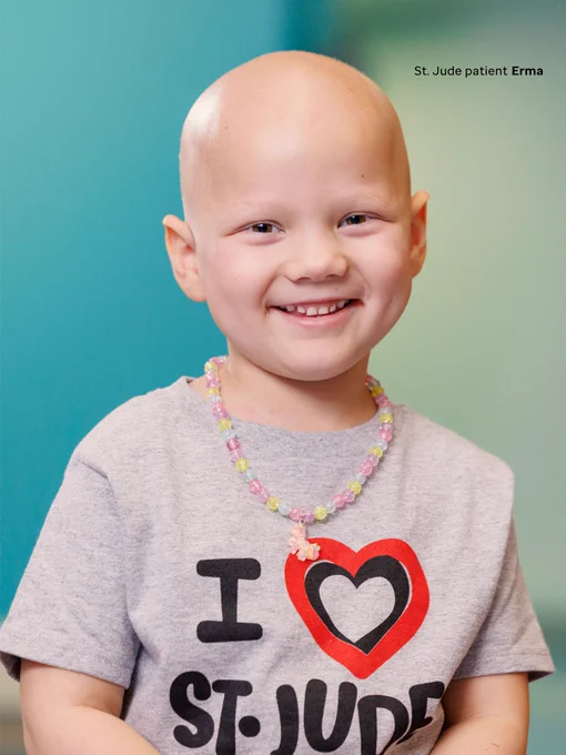 St. Jude patient Erma, pictured smiling at the camera. Her gray shirt reads “I (heart shape) St. Jude”. She is also wearing a necklace.