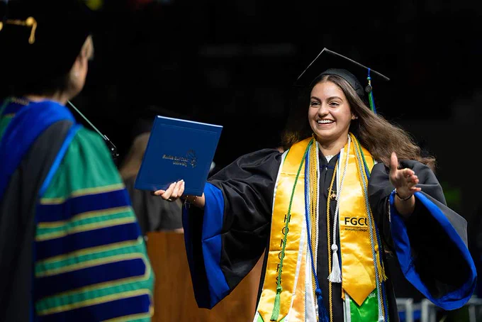 a photo of a graduate holding her diploma frame and walking across the stage smiling