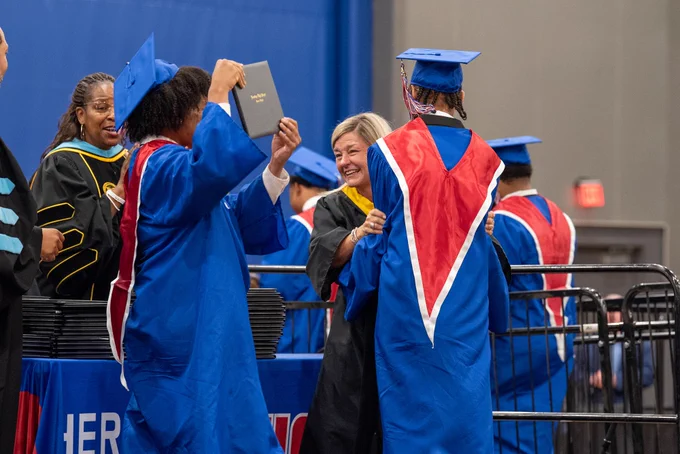 A group of graduates in blue and red graduation gowns and caps stand and talk together.