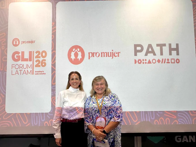 Two individuals stand in front of a screen displaying logos of "pro mujer," "PATH," and "GLIC Forum Latam 2026." They are smiling and dressed in smart casual attire.