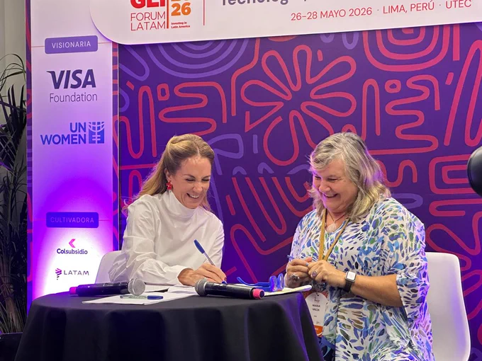 Two individuals are seated at a table with microphones, smiling and engaged in conversation. Behind them is a colorful event backdrop featuring logos of organizations, including Visa Foundation, UN Women, and Latam. The event is the GLI Forum LATAM 2026, taking place in Lima, Peru.