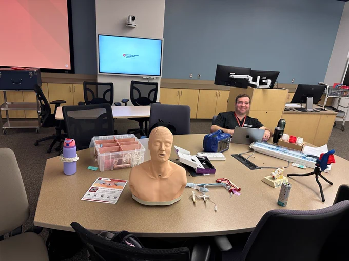 One ENT resident sit around a table with medical training tools and monitors.