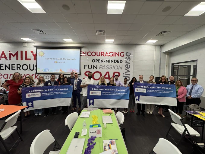People posing with large checks in a room with encouraging messages on the walls.