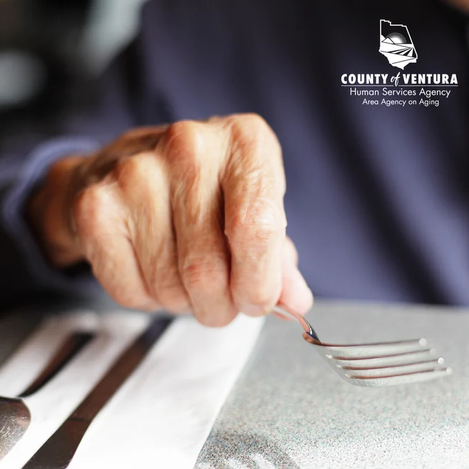 Picture of an older man's hand, holding a fork. VCAAA logo.