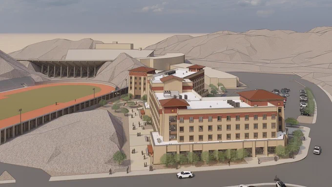 Aerial view of the planned Miner Crossing complex with tan walls and red roofs, nestled in a desert landscape. Adjacent is a Kidd Field with a track-field. Surrounding the structures are hills and parking areas.