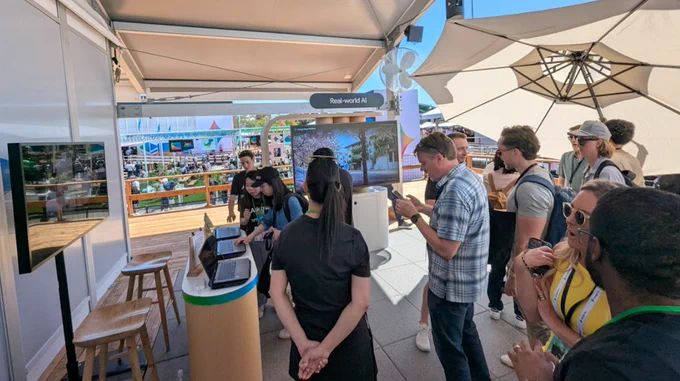 People chat and look at a screen in a booth with a sign reading "real-world AI"
